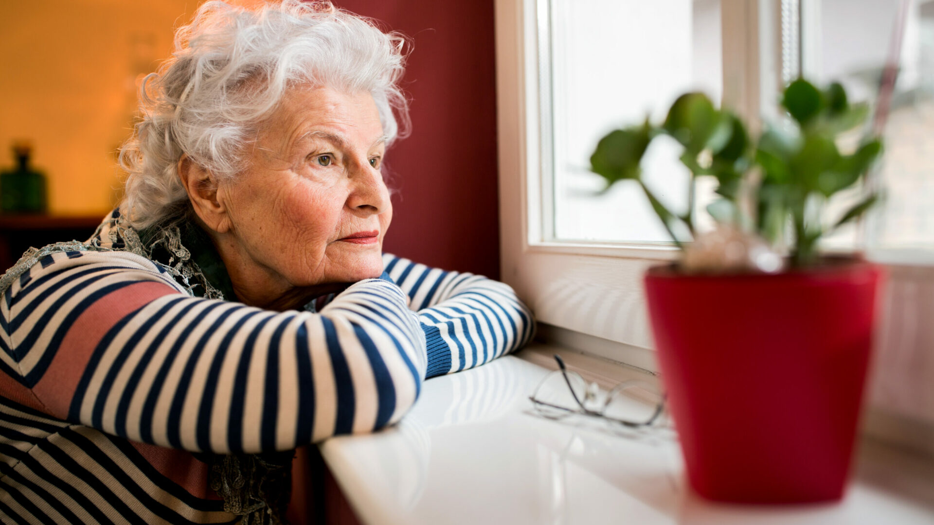 Sad,Alone,Senior,Woman,Looking,Through,Window,At,Home,,Loneliness