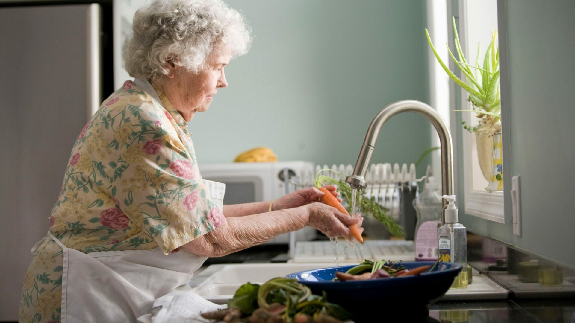 Oudere dame wast groenten in haar keuken