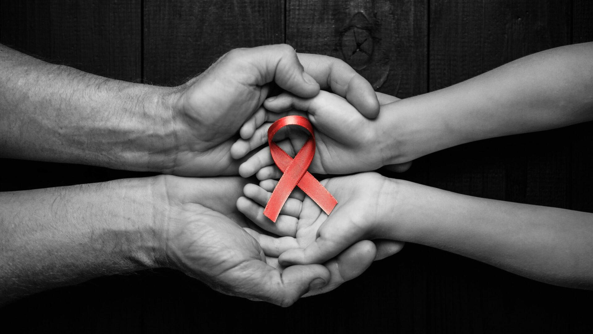 Aid,Red,Ribbon,In,Hands,On,A,Black,Wooden,Background,