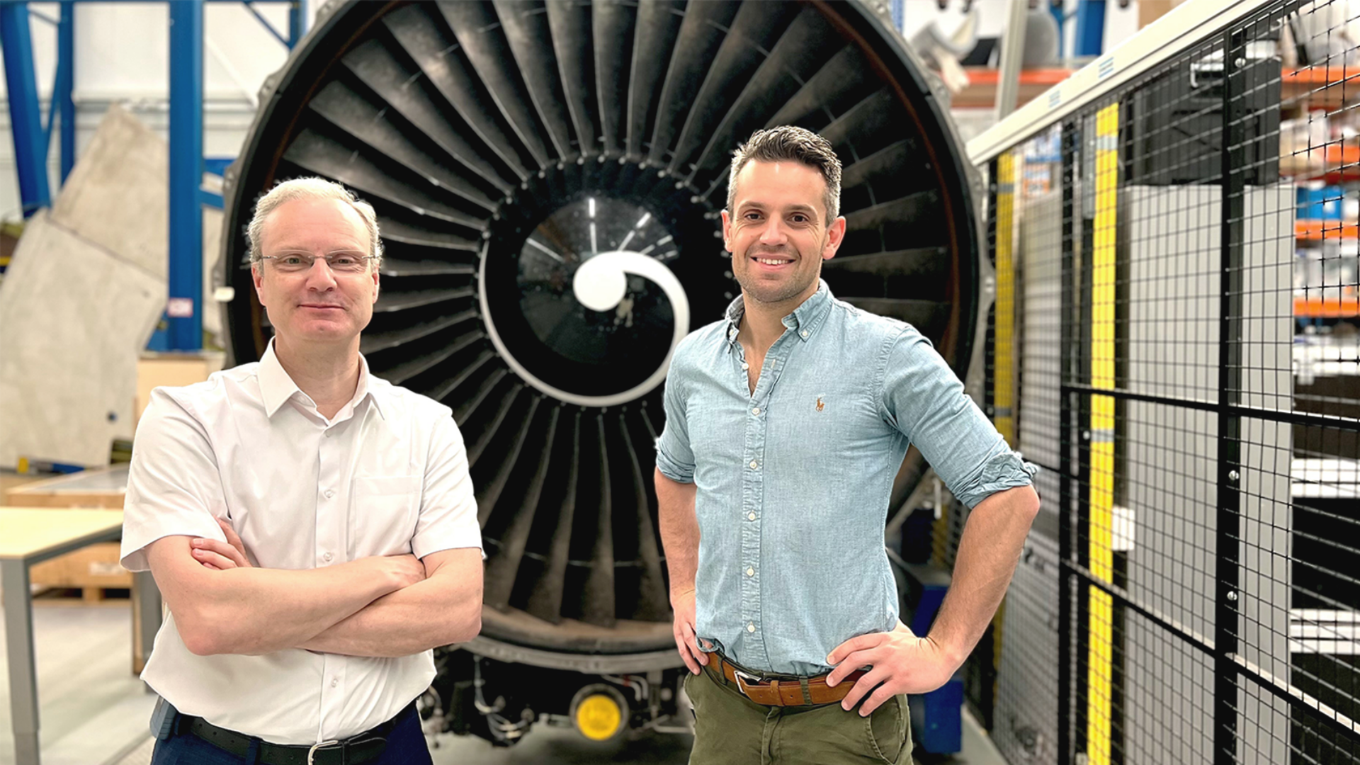 De twee onderzoekers staan voor een grote zwarte vliegtuigmotor op de TU Delft.