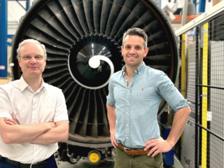 De twee onderzoekers staan voor een grote zwarte vliegtuigmotor op de TU Delft.